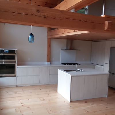 Modern kitchen with light wood cabinetry and stainless steel appliances under wooden beams.