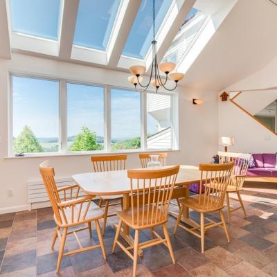 Bright dining area with a wooden table and chairs, large windows, and a purple couch.