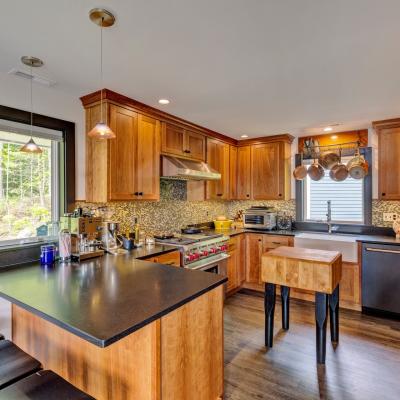 Modern kitchen with wooden cabinets, black countertops, and a view of nature through the window.