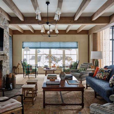 Cozy living room with stone fireplace, wooden beams, and colorful decor. Snow visible outside.
