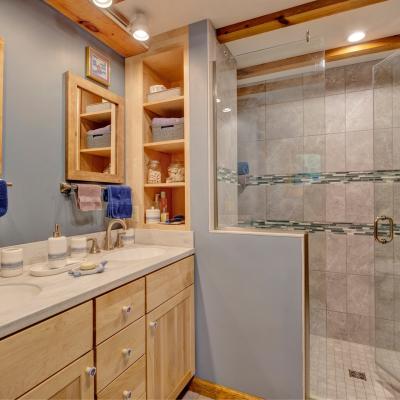 Modern bathroom with double sinks, shower, and wooden accents.