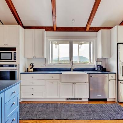 Modern kitchen featuring white cabinets, blue countertop, and mountain view through a window.