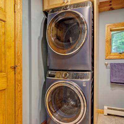 Stacked washer and dryer in a laundry room with wooden accents and a nearby door.