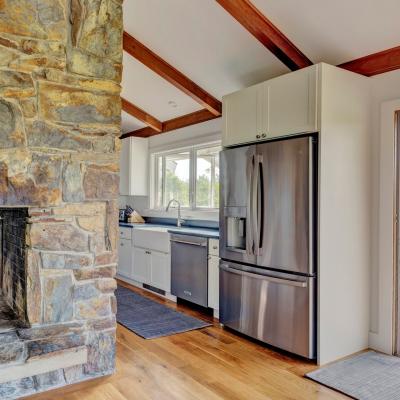 Modern kitchen with stone fireplace, stainless steel appliances, and large windows.