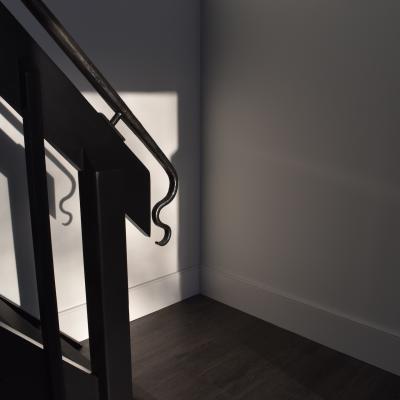 Shadowed staircase corner with a sleek handrail against a light wall.