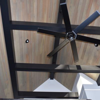 View of a ceiling featuring wooden panels, a large fan, and black structural beams.