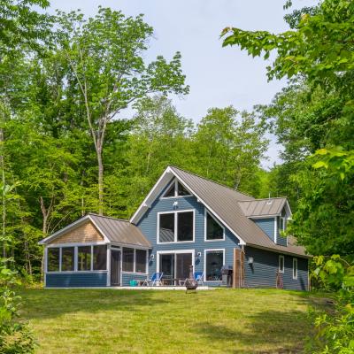 Modern blue house surrounded by lush green trees and grassy landscape.