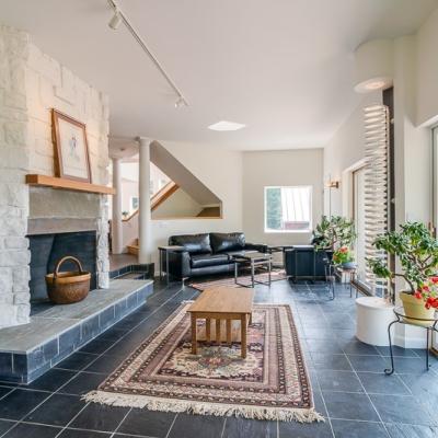 Modern living room with stone fireplace, plants, and natural light from large windows.