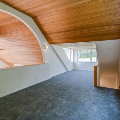 Spacious, modern loft area with wooden ceiling and soft carpet flooring.