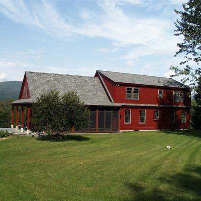 Red house with a gray roof, surrounded by green lawn and trees under a blue sky.