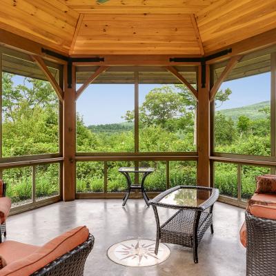 Cozy screened porch with seating and a view of lush greenery and mountains.