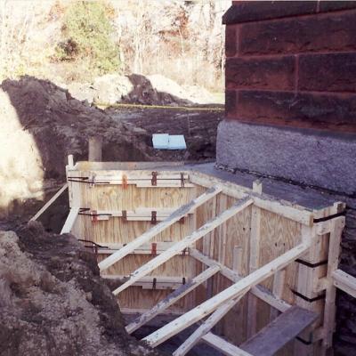 A construction site showing wooden forms for a concrete foundation beside a building.