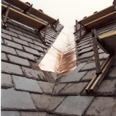 Copper flashing installed between slate roof tiles, viewed from a low angle.