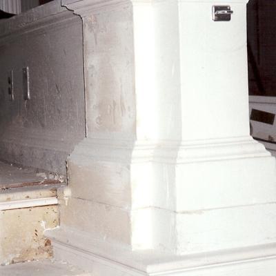 Close-up of a white-painted column and staircase, showing unfinished plaster.