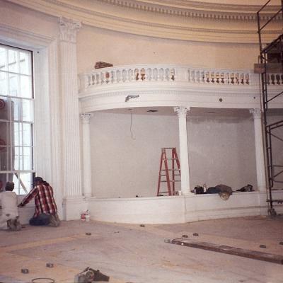 Two workers renovate a room with a large window and scaffolding in the background.