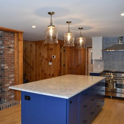 Modern kitchen with blue island, pendant lights, and stone backsplash.