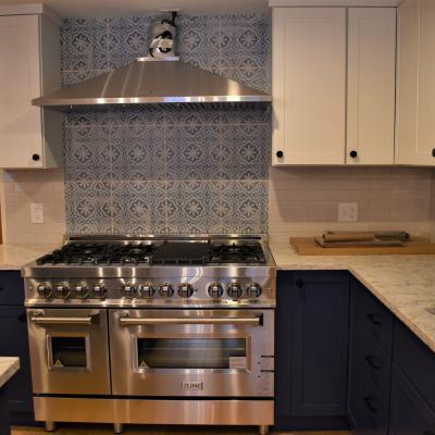 Modern kitchen with stainless steel stove, blue cabinetry, and patterned tile backsplash.