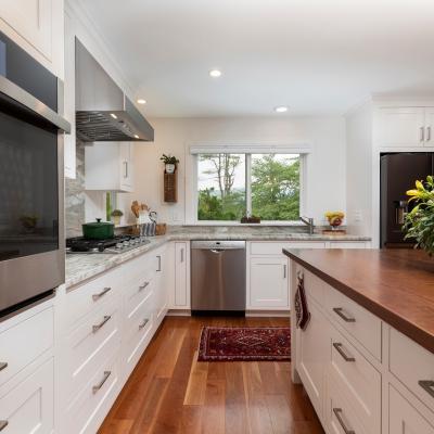 Modern kitchen with white cabinets, granite countertops, and a window view of greenery.