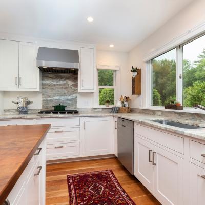 Modern kitchen with white cabinets, granite countertops, and large windows overlooking greenery.