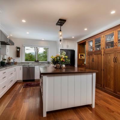 Modern kitchen with a wood island, white cabinetry, and a view of nature through the window.