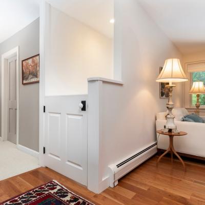 Cozy living space with a white couch, lamps, and a view of a hallway and door.