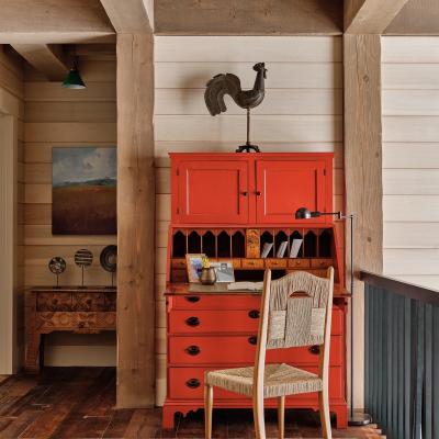 Red writing desk with a chair, artwork, and rustic beams in a cozy interior space.