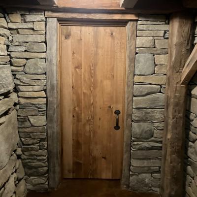 Wooden door with metal handle framed by stone walls and wooden beams, illuminated overhead.