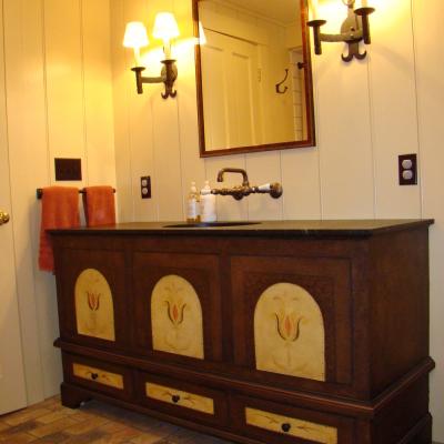 Rustic bathroom with a wooden vanity, mirror, and wall sconces, featuring decorative details.