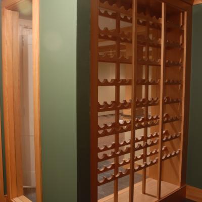 Wooden wine rack in a green-painted alcove, showcasing multiple slots for bottles.