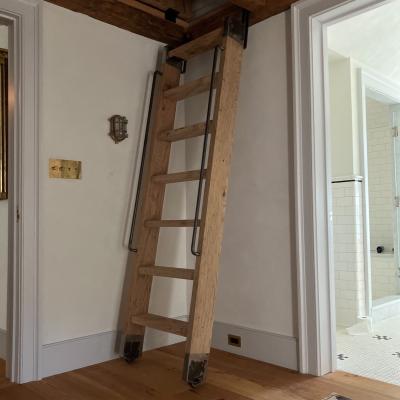 Wooden ladder against a wall leading up to a loft space in a room with hardwood floors.