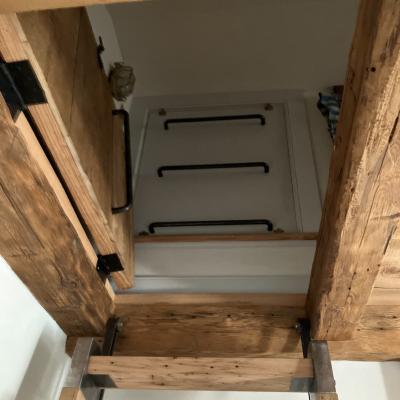 View looking up at a wooden staircase leading to a closed door with handles.