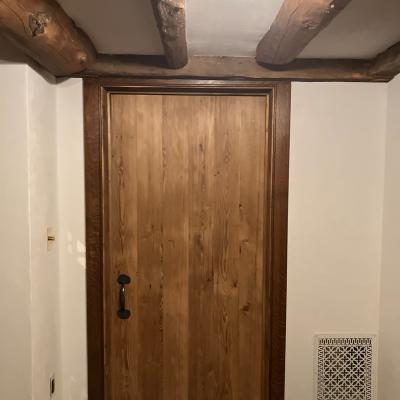Wooden door with metal handle, set in a cozy room with exposed beams and a vent.
