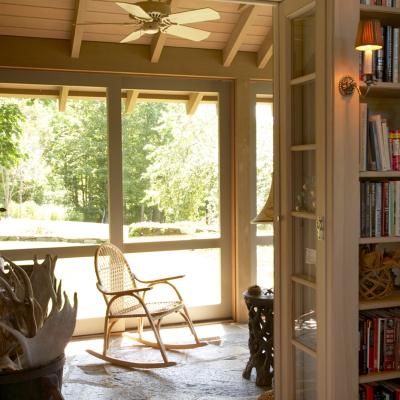 Light-filled interior with a rocking chair, bookcase, and view of the outdoors.