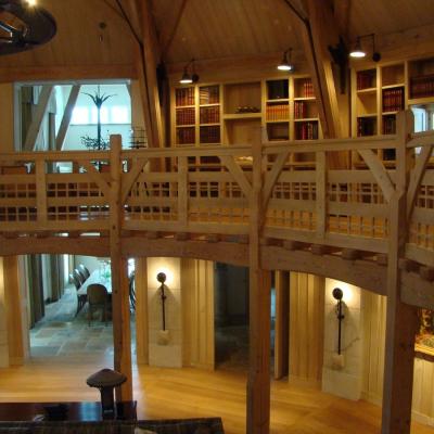Wooden balcony overlooking a spacious, well-lit interior with bookshelves and furnishings.