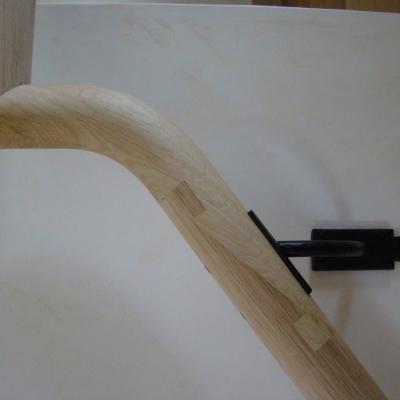 Curved wooden handrail with a black metal bracket mounted on a light surface.