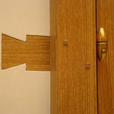 Wooden door joint with a distinctive cutout design and a gold-colored hinge.