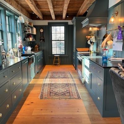A stylish kitchen featuring dark cabinets, wooden beams, and a vintage rug.