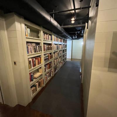 Narrow hallway lined with bookshelves, leading to a door at the far end.