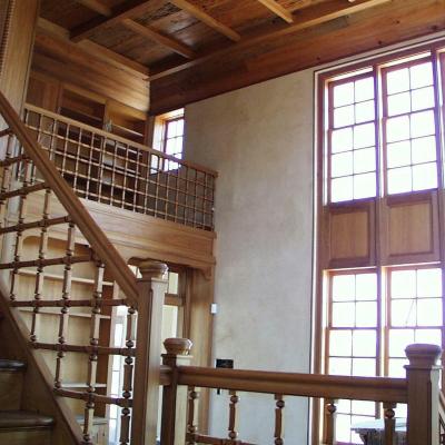 Interior of a wooden staircase with decorative railings and large windows.