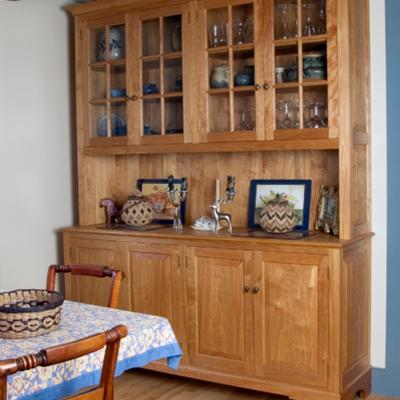 Wooden cabinet with glass doors displaying dishes, next to a dining table and chairs.