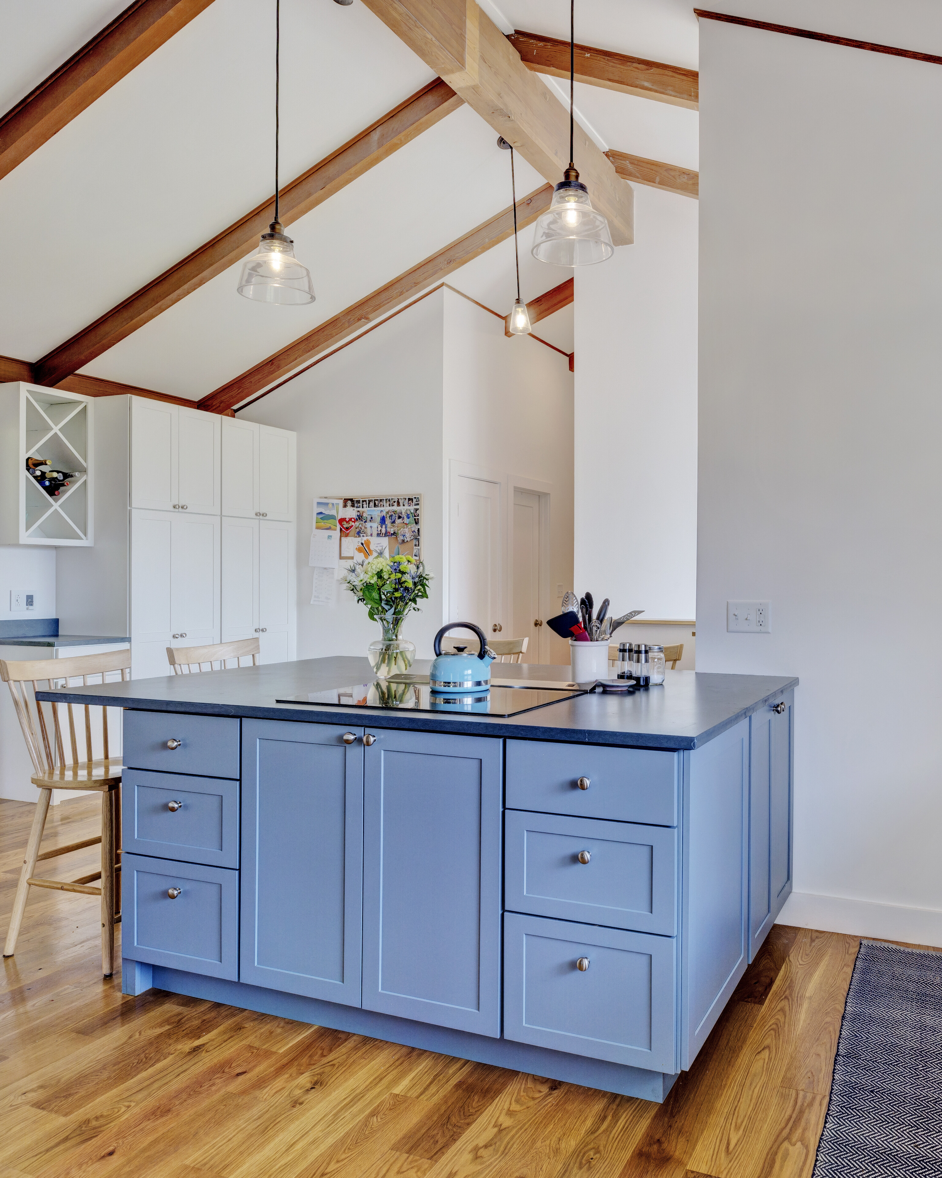 Light-filled kitchen with a blue island, wooden beams, and modern decor.