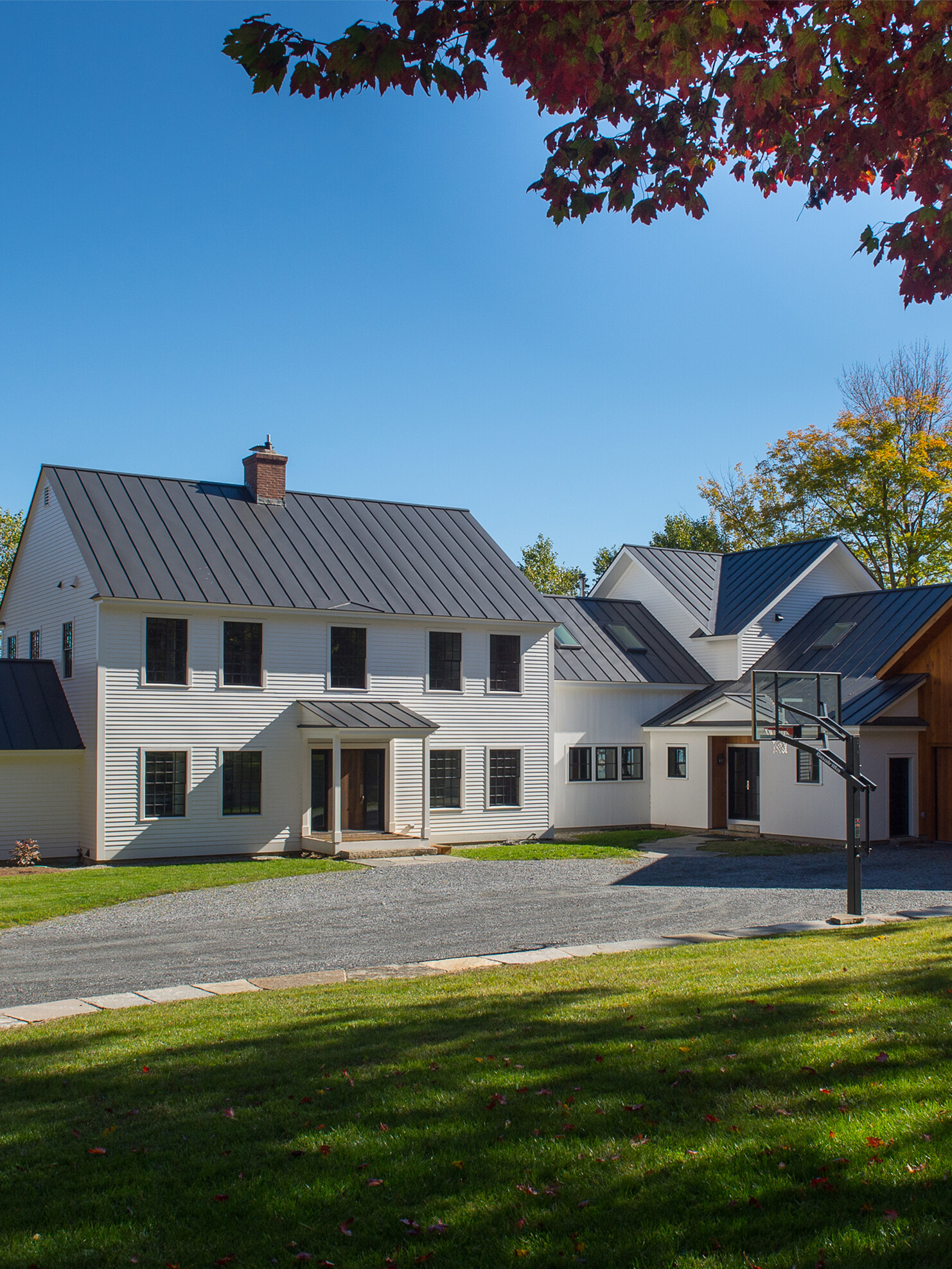 Modern white house with metal roof, basketball hoop, and green lawn under a clear blue sky.