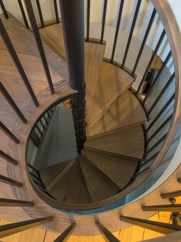 Spiral staircase with wooden steps and black railings viewed from above.