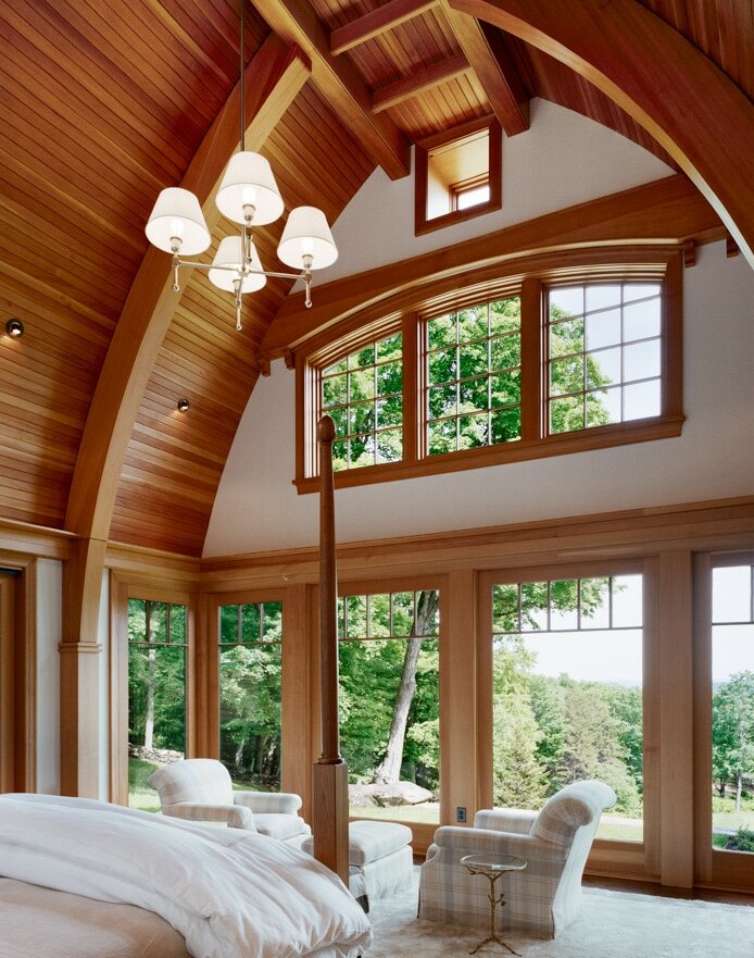 Cozy bedroom with wooden beams, large windows, and comfortable seating overlooking nature.